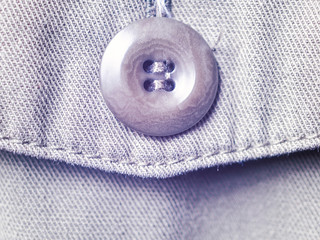 The button is sewn on the flap of a khaki jeans jacket pocket. The fabric texture is clearly visible.