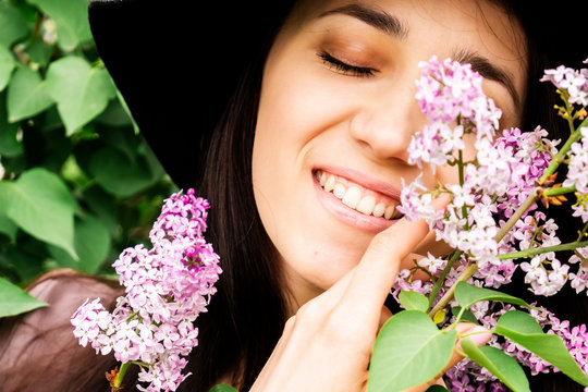 Beautiful young Russian woman hugs a branch of lilac smiling closing her eyes. Beautiful photo of a brunette near a lilac. Girl in the bushes of lilac.