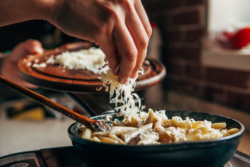 Female hand sprinkles grated cheese on a pan with pasta - obrazy, fototapety, plakaty