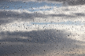Raindrops on the window glass on blurred background of cloudy sky. Beautiful water drops, rainy weather in town
