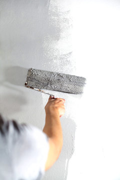 Human hand with large roller of paint begins to paint a white wall handicraft master painter training contrast color sample color test tool renovation gray silver craftsman