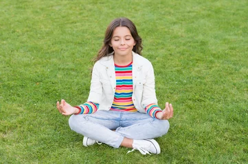  kid meditating in yoga pose on grass. child in lotus pose on green grass. Concept of calm and meditation. meditation in nature. peace and relax. small girl meditate in summer park. healthy lifestyle © be free