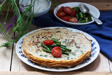 Nettle and spinach pancakes served with sour cream sauce, tomatoes and asparagus. Rustic style.