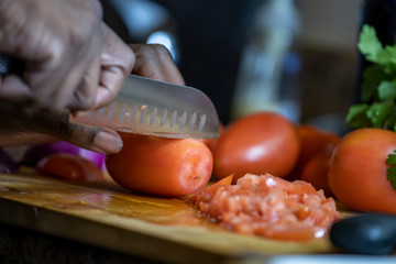 close up view African american woman hand cutting tomatoes into thin slices for healthy and nutritious meal lifestyle. the organic meal the culinary chef is making is delicious