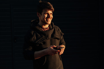 Happy smiling young man using modern smart phone while standing at crosswalk at the sunset in city center