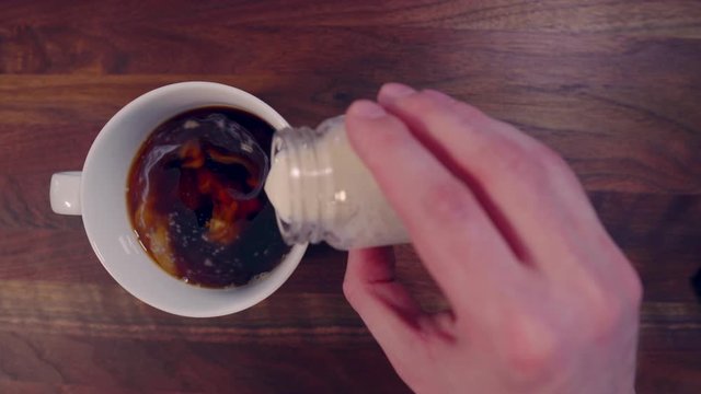 Hand Pouring Coffee Creamer Into Black Coffee From Overhead