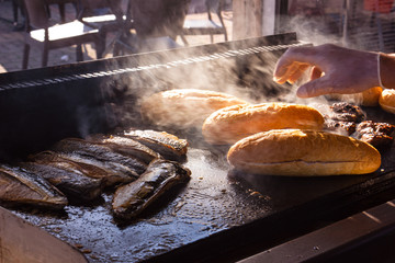 Components of Turkish Balyk kebab are fried on a street grill: bread, fish and vegetables. Fishburger objects are blurred by sunlight passing through the smoke. Glare and flare. Selective focus