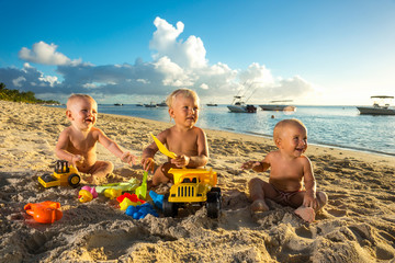babies play with toys on the sand against the background of the transparent ocean and snow-white yachts