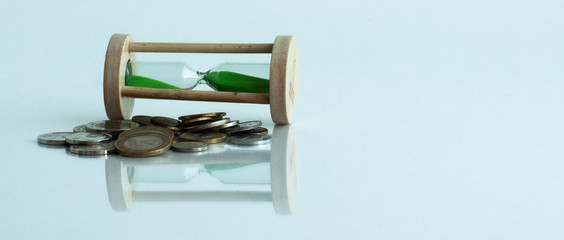 Hourglass and coins on a white background and reflection in a mirror surface.