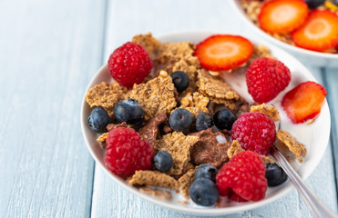 Granola with blueberries and raspberries in white bowl on dark white desk.