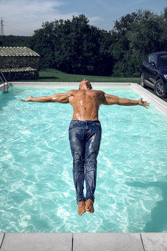 Muscular Young Sexy Wet Naked Guy Falls Into The Pool In Blue Jeans Outdoors. Athletic Tanned Man Resting On Vacation.