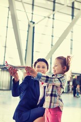 Portrait of airport staff holding airplane toy while playing with cute little girl in airport
