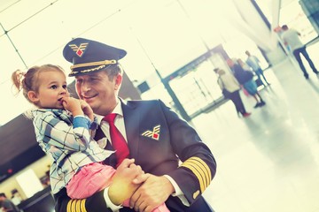 Portrait of mature pilot carrying cute little child in airport
