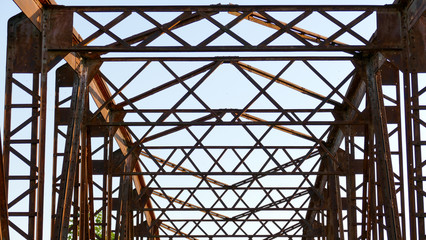 An old disused rusted brown bridge in the countryside connecting two banks across a river, formerly used for busy agricultural traffic