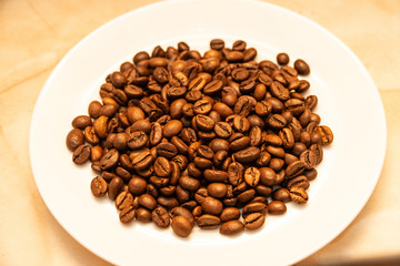Roasted coffee grains lie on a white plate. Making a coffee drink.