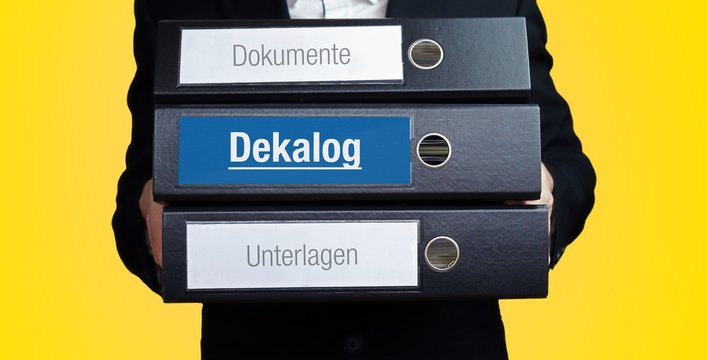 Dekalog. Anwalt im Anzug tr&auml;gt einen Stapel Ordner. 3 Aktenordner. Blaue Beschriftung mit Text. Hintergrund gelb. Recht, Gesetz, Rechtsprechung