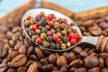 A spoon with a wooden handle with spices lies roasted coffee beans on a blue wooden background.
