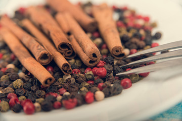 Cinnamon and spices lie on a white plate, a fork lies nearby. Cinnamon and spice grains closeup.