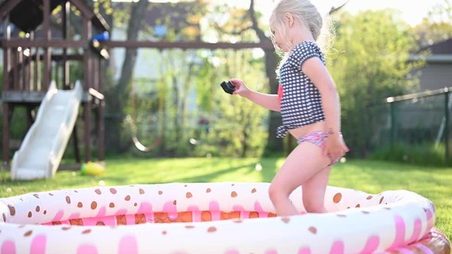 little girl playing in inflatable kiddie pool outside in backyard in summertime
