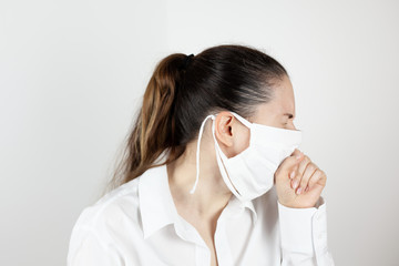 A young girl in a mask coughs and covers her face with her hand out of habit. Demonstration of habits. Life during the pandemic. The first signs of the disease.