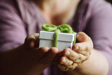 Hände halten eine kleine weiße Schachtel mit einer grünen Schleife. Ein Geschenk, geringe...