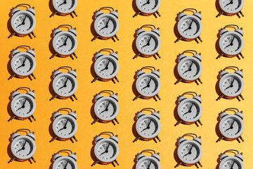 White retro alarm clock pattern on orange yellow background. Creative minimal time, school, business, morning, deadline concept. Top view, flatlay, layout.