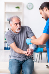 Fototapeta premium Young male doctor and old patient in first aid concept