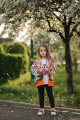 Cute little girl stand in front of flowering tree. Petals blows away like snow. Beautiful white blooming tree