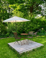 Wunderschöner Garten im Einfamilienhaus mit kleinem Tisch und Stühlen und Sonnenschirm mit der Sonne im Hintergrund