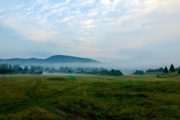 Fototapeta premium Fog in the village at sunrise over the fields and over the mountain