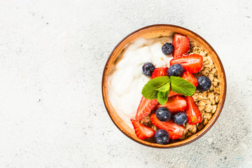 Greek yogurt granola with fresh berries on white stone table.