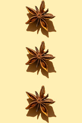 Three brown anise stars of imperfect shape with sunny shadows isolated on light yellow vertical background. Creative art pattern of spicies