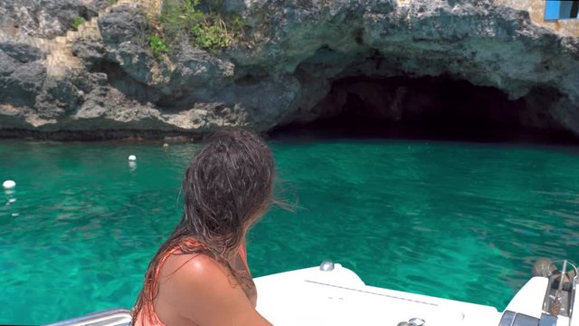 Young woman sitting on boat approaching towards cave, female tourist exploring on sunny day - Montego Bay, Jamaica
