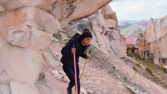Slow motion of woman hiking with poles by rock formation, tourist exploring mountain - Rainbow Mountain, Peru