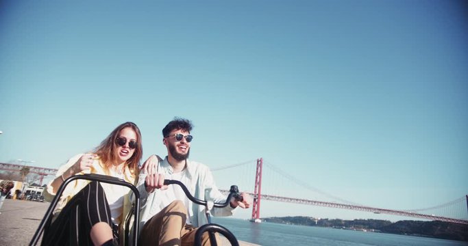 Blonde woman and middle-eastern man riding sidecar bicycle by riverside