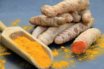 Turmeric powder in a wooden spoon and roots on a dark table (curcuma longa), Kurkuma