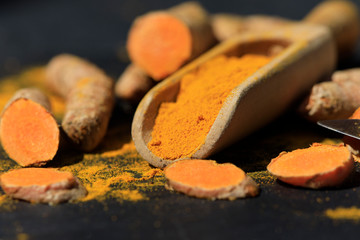 Turmeric powder in a wooden spoon and roots on a dark table (curcuma longa), Kurkuma
