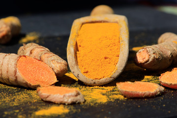 Turmeric powder in a wooden spoon and roots on a dark table (curcuma longa), Kurkuma