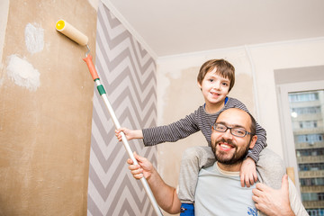 Cheerful father and son hanging wallpaper together, home renovation, fun