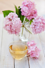 Phloxes. A still life with a bouquet of pink phloxes in a transparent vase and cup of herbal tea against a wooden background. Selective focus.