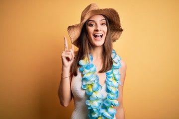 Young beautiful brunette woman on vacation wearing swimsuit and Hawaiian flowers lei pointing...
