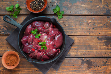 Raw chicken livers with pepers in a skillet on wooden background