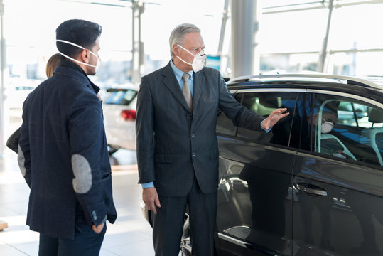 Young Family Talking To The Salesman And Choosing Their New Car In A Showroom During Coronavirus Pandemic