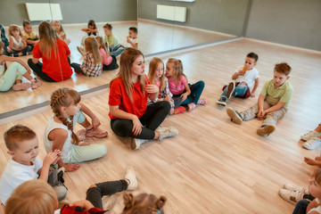 Giving advice. A group of little dancers sitting on the floor gathered around their female dance teacher. Full length portrait of young female dance teacher talking to group of little girls and boys