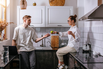 married caucasian couple spend morning together in the kitchen, they use laptop, work and talk at...