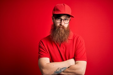 Young handsome delivery man wearing glasses and red cap over isolated background skeptic and nervous, disapproving expression on face with crossed arms. Negative person.