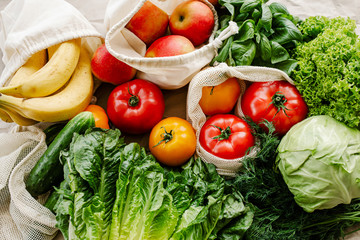 Fresh vegetables and fruits in eco cotton bags on table in the kitchen.