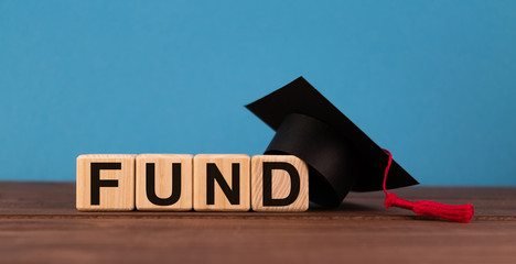 Word FUND on wooden cube blocks on wood table with graduation hat on blue background. Financial,...