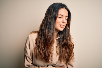 Young beautiful brunette woman wearing casual shirt standing over white background with hand on stomach because nausea, painful disease feeling unwell. Ache concept.