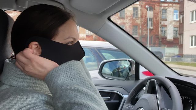 Brunette woman driver wearing medical face mask behind the wheel of her car during COVID-19 coronavirus pandemic.